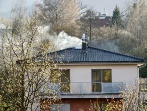 A two-story house with a tiled roof emits white smoke from a chimney
